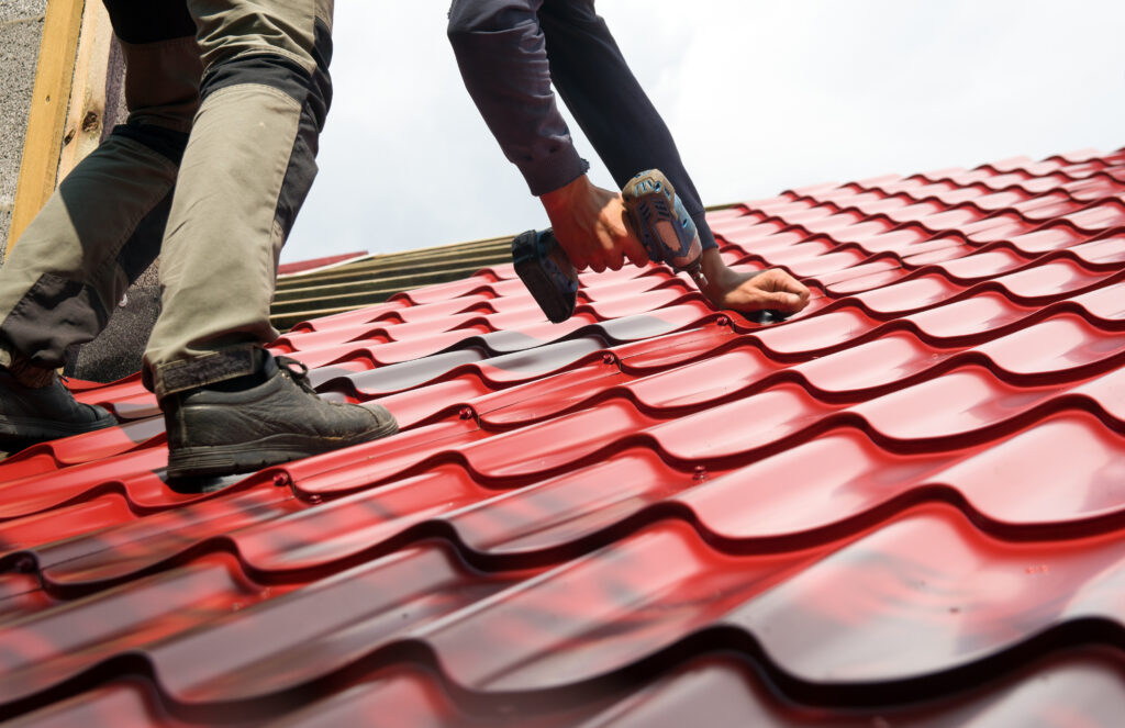 Couvreur vissant des panneaux métalliques rouges à l'aide d'une perceuse — couvreur pour une toiture métallique.