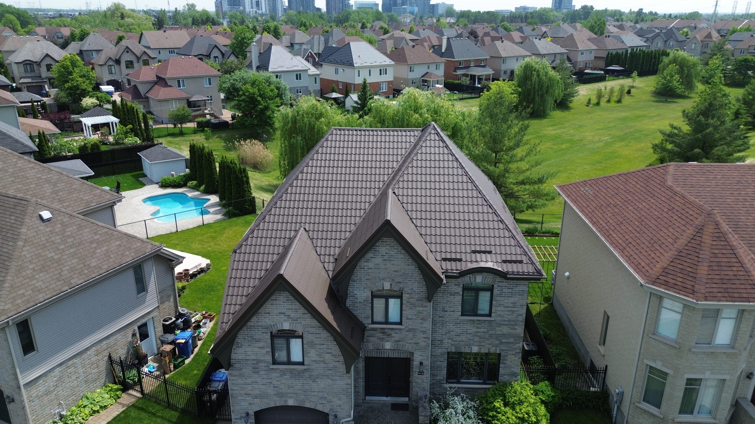 Vue drone d'une résidence en pierre avec toiture en tuiles métalliques brun foncé en été — exemple de garantie d’une toiture métallique.