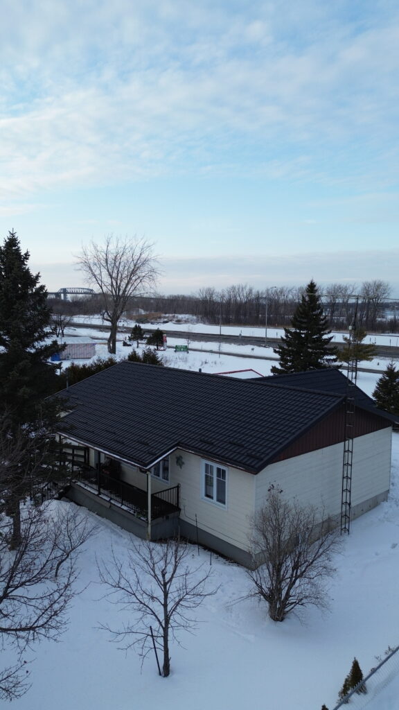 Vue drone d'une maison blanche avec toiture métallique noire sous la neige en hiver — saison pour refaire sa toiture.