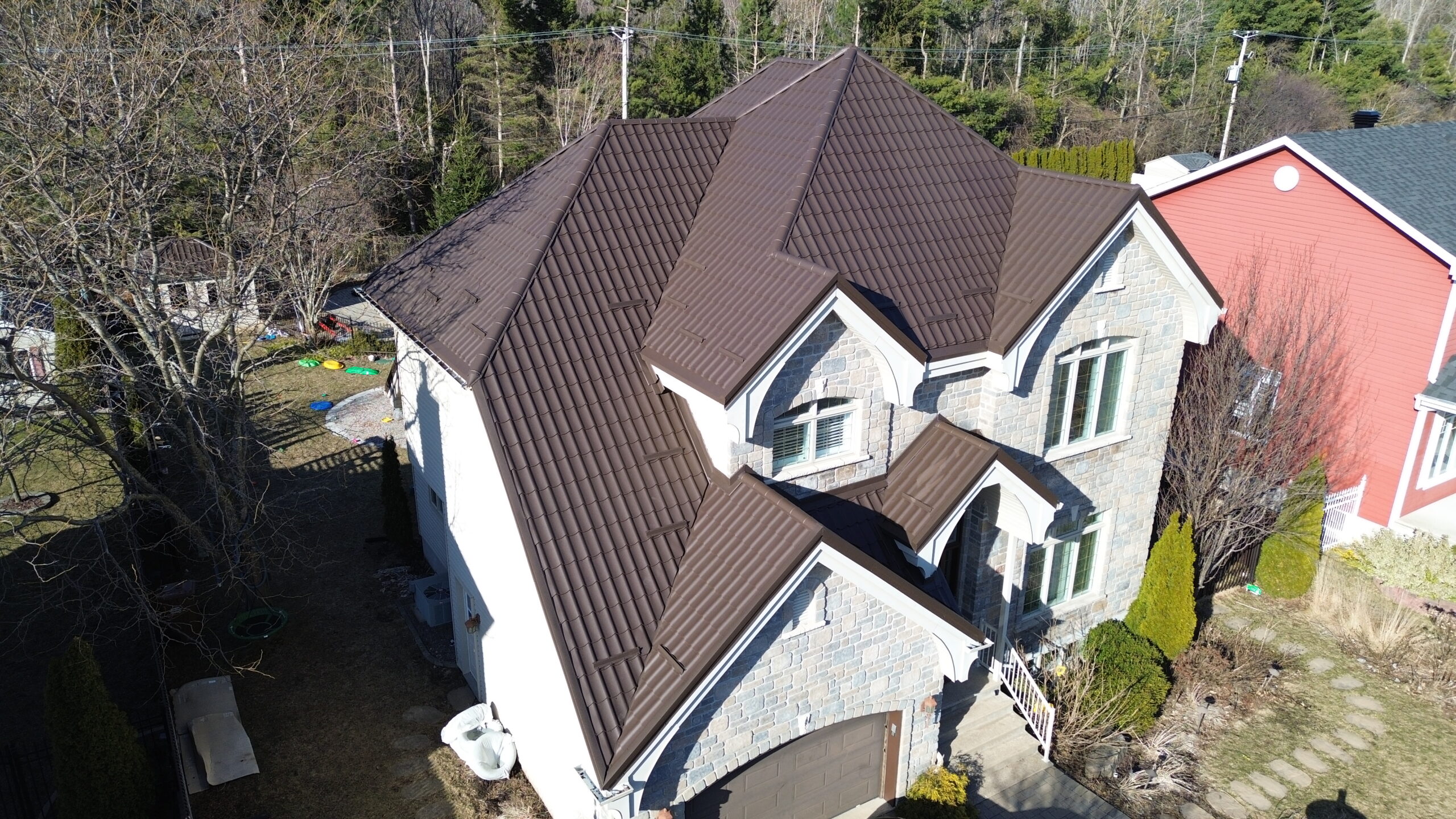 Vue aérienne d'une maison en pierre avec toiture métallique brun chocolat au début du printemps — saison pour refaire sa toiture.