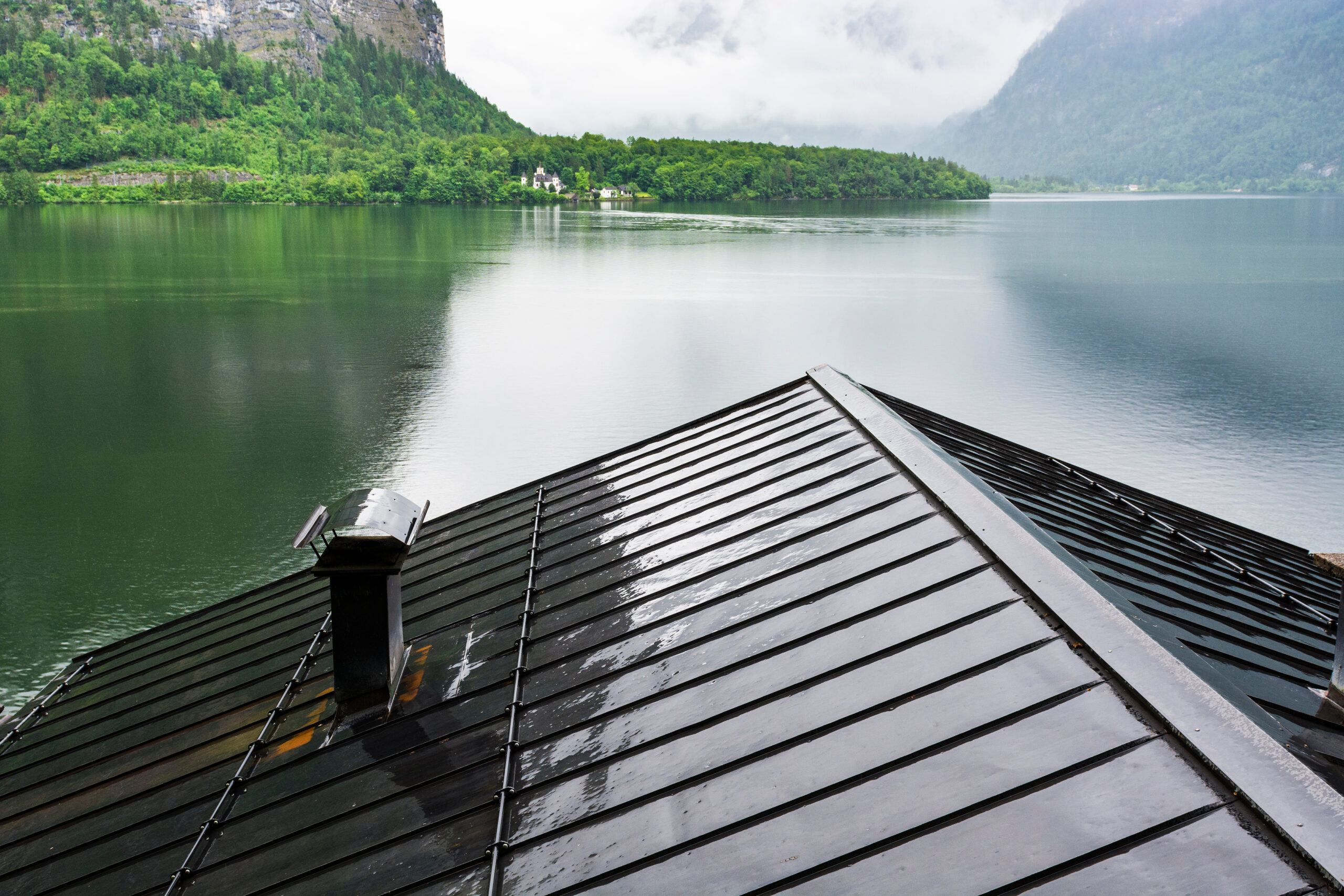 Toit en métal noir mouillé sous un ciel nuageux avec vue sur un lac — toit en métal et bruit de pluie.