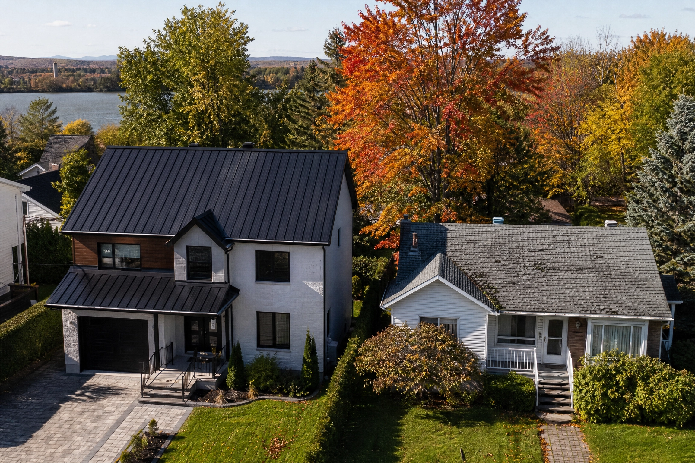 Rentabilité d'un toit en métal : vue aérienne d'une maison au toit métallique noir à côté d'une maison au toit en bardeaux, en bord de rivière à l'automne