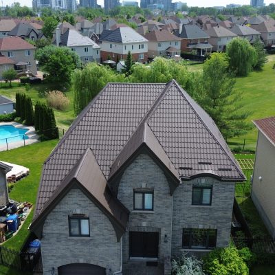 Vue drone d'une résidence en pierre avec toiture en tuiles métalliques brun foncé en été — exemple de garantie d’une toiture métallique.
