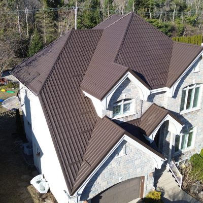 Vue aérienne d'une maison en pierre avec toiture métallique brun chocolat au début du printemps — saison pour refaire sa toiture.