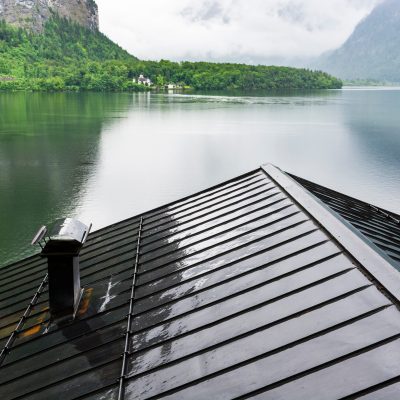 Toit en métal noir mouillé sous un ciel nuageux avec vue sur un lac — toit en métal et bruit de pluie.